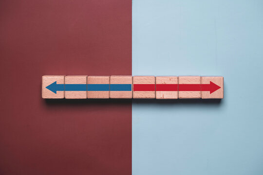 Political polarization concept with opposing arrows on wooden blocks, representing ideological division, conflicting opinions, public debate, democracy, social conflict, and political disagreement.