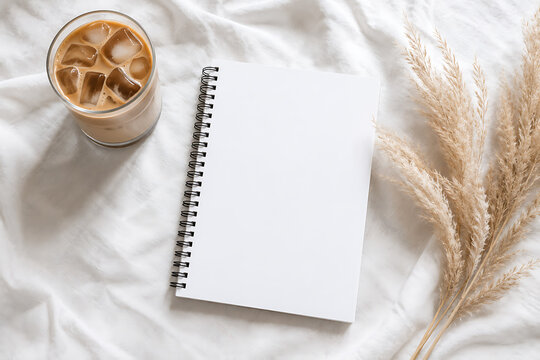 Minimalist blank notebook mockup on white bed sheets, iced coffee latte in glass, dried pampas grass decor, aesthetic morning journaling concept isolated on White Background ai