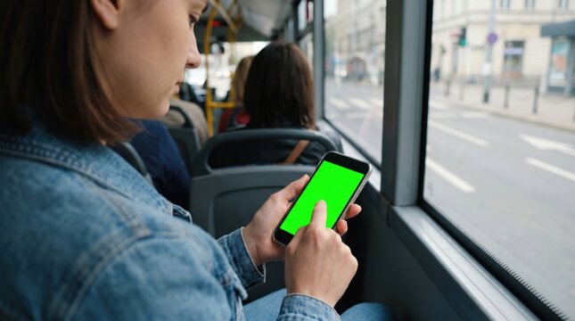 Woman holding smartphone with green screen in public bus. Passenger using mobile cell phone device for navigation during trip. Concept of digital lifestyle, wireless technology and city commute.