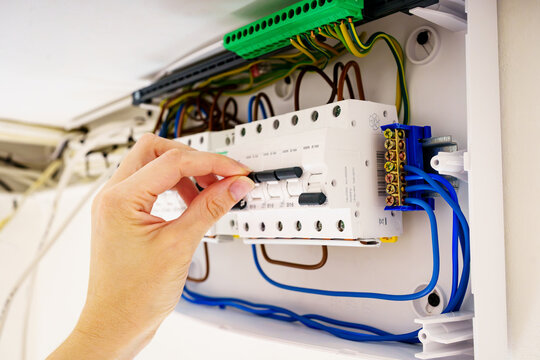Closeup of a hand switching a toggle on an electrical consumer unit. Detailed side view of modern domestic breaker panel with visible colorful wiring during maintenance or repair.