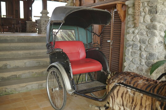 Vintage Traditional Asian Three-Wheeled Pull Cart with Red Upholstered Seat and Black Canopy Parked on a Stone Terrace