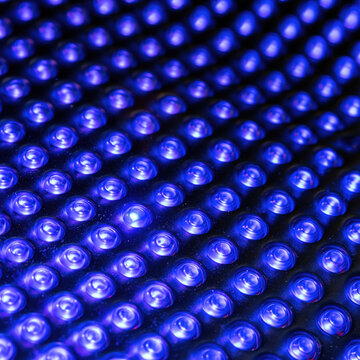 Extreme close up of a blue LED therapy panel with glowing circular diodes arranged in a precise grid for medical and wellness technology backgrounds