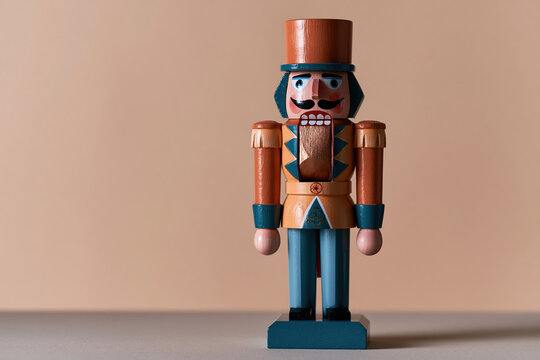A traditional wooden nutcracker soldier in a blue and gold uniform stands against a beige background for Christmas greeting cards and holiday product catalogs