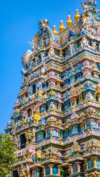 Close-up view of the richly ornamented Dravidian-style gopuram of Arulmigu Thirumarainatha Swamy Temple, showcasing intricate Hindu sculptures and colorful architectural details against a clear blue s