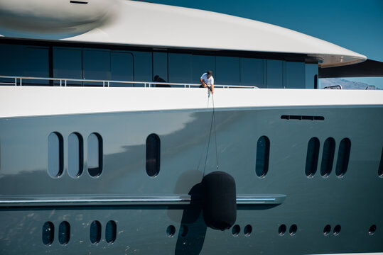 Detail of beautiful Superyacht, deckhand lifting the huge fender of the starboard side of the megayacht, spotless grey and white superstructure