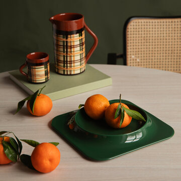 Rustic ceramic plaid pitcher and mug set with fresh citrus fruits on a light table with warm ambiance