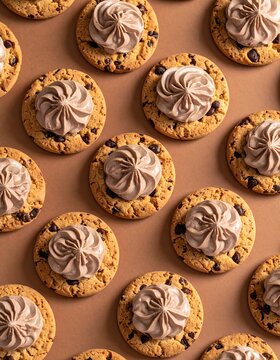 A pattern of chocolate chip cookies with brown frosting topping on a beige background
