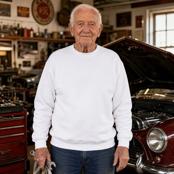 Mechanic stands in a garage workshop holding a wrench with a classic car in the background.
