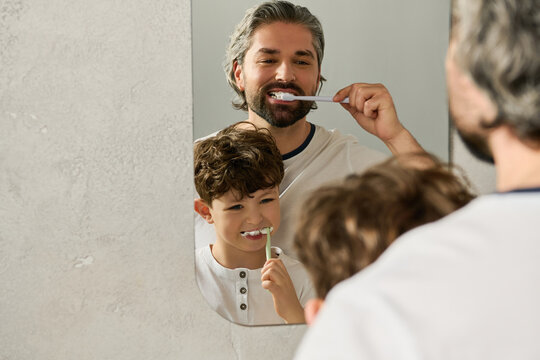 Father and son joyfully brushing teeth together in a bright, cheerful bathroom