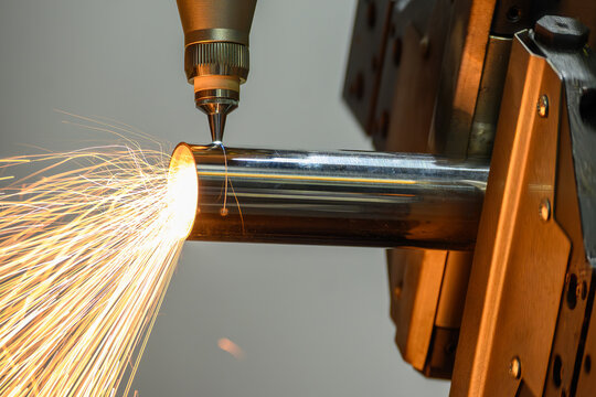 Operation of a high-power fiber laser cut machine cutting a stainless steel tube with sparkling light.