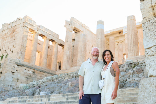 Couple smiling at the ancient Acropolis in Athens, Greece, surrounded by historic marble columns and warm summer light.