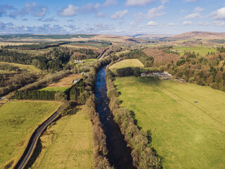 Obraz premium The River Esk winds through green fields and dense trees near Langholm in the Scottish Borders. This scene shows a clear view of the landscape near Langholm on the A7