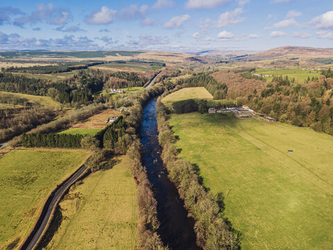 The River Esk winds through green fields and dense trees near Langholm in the Scottish Borders. This scene shows a clear view of the landscape near Langholm on the A7