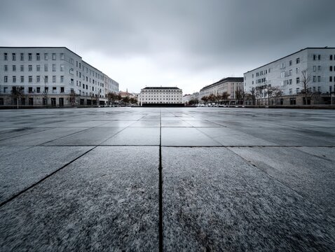 Vast empty city plaza framed by architecture under an overcast sky