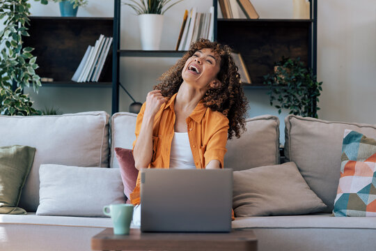 Beautiful woman celebrating something while working with laptop sitting at home