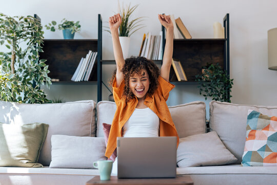 Beautiful woman celebrating something while working with laptop sitting at home