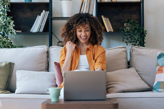 Beautiful woman celebrating something while working with laptop sitting at home