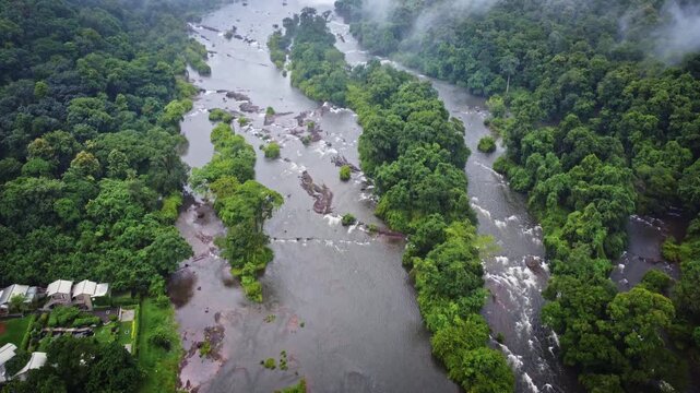 Aerial drone reveal of Athirappilly Waterfalls flowing through dense tropical rainforest during the monsoon season in Kerala, India, showcasing the spectacular landscape of the Western Ghats.