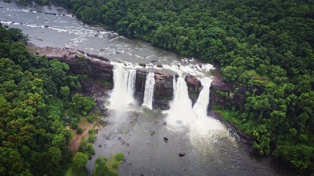 Aerial drone view of Athirappilly Waterfalls surrounded by lush rainforest and monsoon clouds in Kerala, India, showcasing the spectacular beauty of the Western Ghats.