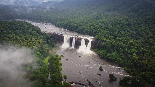 Aerial drone view of Athirappilly Waterfalls surrounded by lush rainforest and monsoon clouds in Kerala, India, showcasing the spectacular beauty of the Western Ghats.