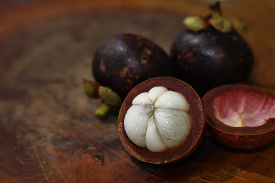 Tropical Fruit,Healthy Eating,Copy Space,Healthy Lifestyle,fresh mangosteen,purple mangosteen,cut open fruit,white segments,edible flesh,wooden cutting board,rustic background,exotic food,organic prod