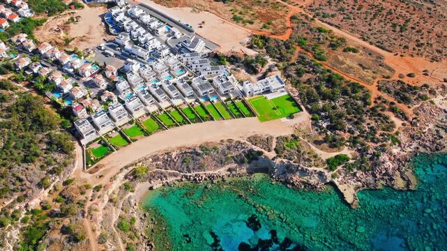 Drone view of Konnos Bay resort area in Cyprus. Beachfront buildings, rocky coastline and blue Mediterranean water form a scenic coastal view.