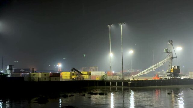 Illuminated industrial dockyard at night with cranes and containers under bright lights