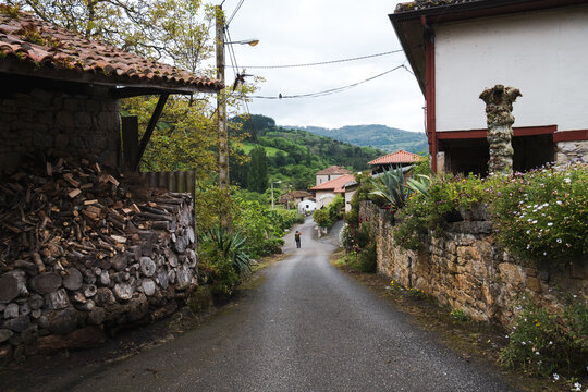 Narrow asphalt street winding through a traditional rural village with stone houses on the Camino Primitivo.