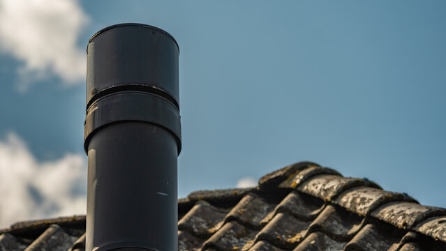 Black metal chimney pipe on weathered roof against blue sky