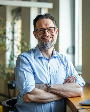 Mature businessman smiling confidently with arms crossed in modern office