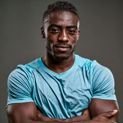 Obraz premium Athletic Man Portrait: A confident black man with muscular arms folded across his chest, looking directly at the camera with a determined expression. He wears a light blue t-shirt.