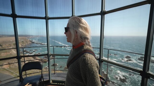 A mature woman walks around the inside of Point Arena Lighthouse looking out at the Pacific Ocean enjoying the view with a smile.