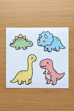 A set of four cute pixel art dinosaur stickers in soft pastel colors including green blue yellow and pink placed on a white sheet over a textured wooden background.