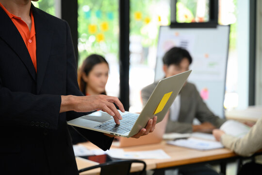 Close Up of Business Leader Holding Laptop During Team Meeting in Modern Office with Whiteboard