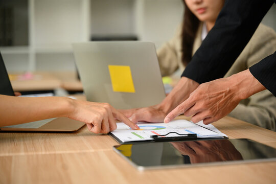 Business colleagues reviewing financial charts and graphs on clipboard during office meeting with laptops on desk