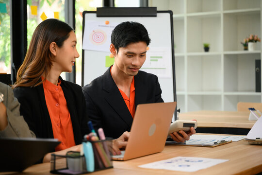Asian Business Colleagues Collaborating on Laptop in Modern Office with Strategy Whiteboard