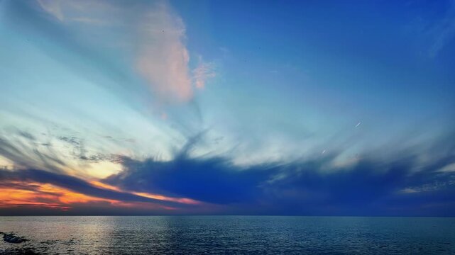 Timelapse over batumi shows a fiery sunset glow fading behind streaked clouds and calm sea.