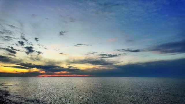 Timelapse of a vivid sunset glowing over a calm marine horizon with drifting clouds.