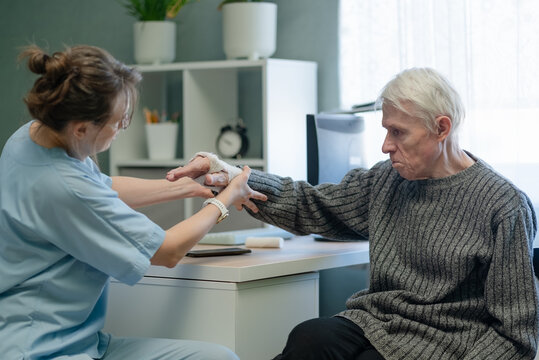 Nurse assisting elderly man with injured hand therapy at hospital. Healthcare professional guiding senior patient through hand exercise with gentle care and attentive support indoors
