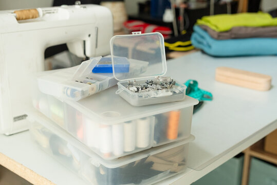 Presser feet organized in a storage container on a table for sewing machine accessory collection. Notions and accessories stored with neat professional care indoors in a home craft room.