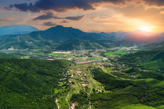 Golden sunset light illuminates the green mountains and winding river valley within the rural countryside of Vietnam during a calm and clear summer evening