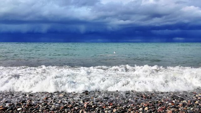 Dramatic dark storm clouds loom over the turquoise black sea horizon near a pebble shore.