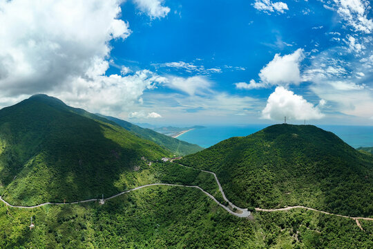Curving road passes through vibrant green tropical mountains that overlook the blue ocean coastline of Vietnam on a beautiful afternoon under clear skies
