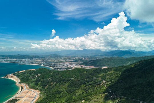 Lush green mountains slope toward the blue sea near a coastal town in Vietnam under a bright sunny sky with fluffy white clouds during the daytime