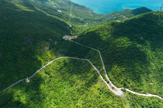 Curvy road snakes through the dense tropical jungle terrain on the mountainside near the ocean coast during a sunny day with natural light and shadows