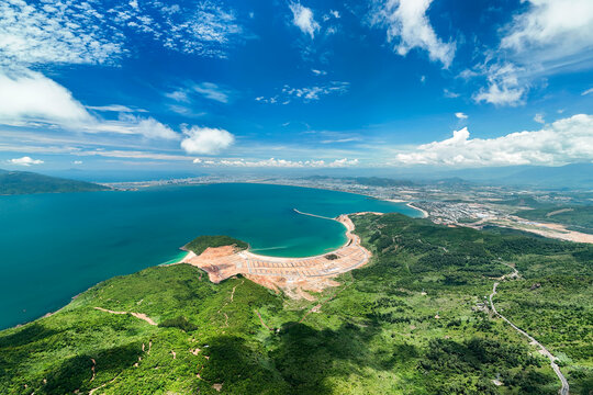 Beautiful tropical coastline showing lush mountain terrain meeting the calm blue waters of the ocean under a bright summer sky with scattered white clouds