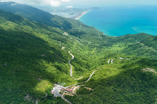 Mountain road stretching across green hills toward the clear blue ocean during a clear day in Vietnam with lush jungle vegetation covering the landscape