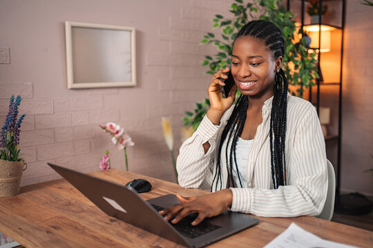 Smiling woman making phone call while working on laptop