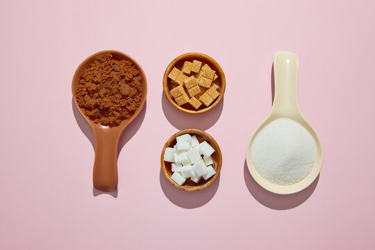 Assortment of sugar on pink background. Muscovado, white crystal sugar, white sugar cubes and brown sugar cubes.