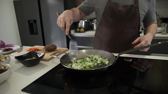 Chef wearing an apron stir frying chopped vegetables in a steel wok on an induction cooktop